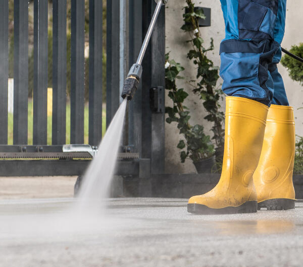 Man in yellow gumboots pressure washing a driveway